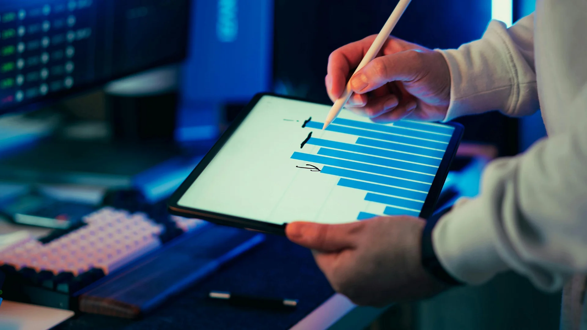 A person using a stylus to adjust a digital bar graph on a tablet. The setting is a dimly lit workspace, creating a focused, analytical atmosphere.